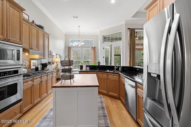 kitchen with crown molding, decorative light fixtures, light wood-type flooring, a kitchen island, and stainless steel appliances