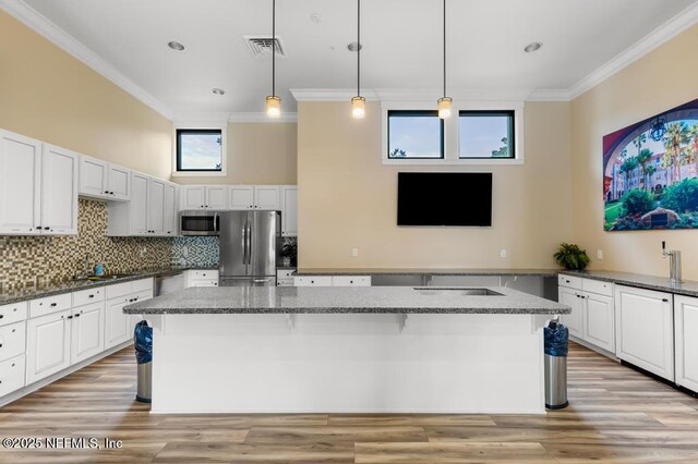 kitchen with stainless steel appliances, decorative light fixtures, a center island with sink, and dark stone counters