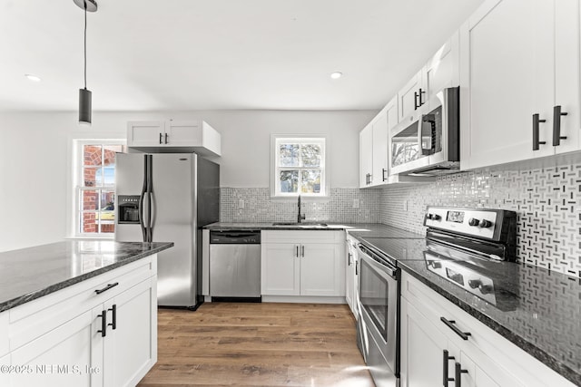 kitchen featuring appliances with stainless steel finishes, decorative light fixtures, white cabinetry, sink, and dark stone counters