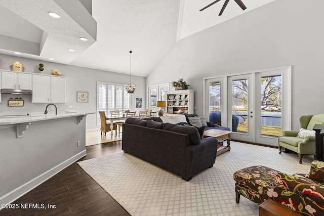 living room featuring ceiling fan with notable chandelier, high vaulted ceiling, a textured ceiling, and light wood-type flooring