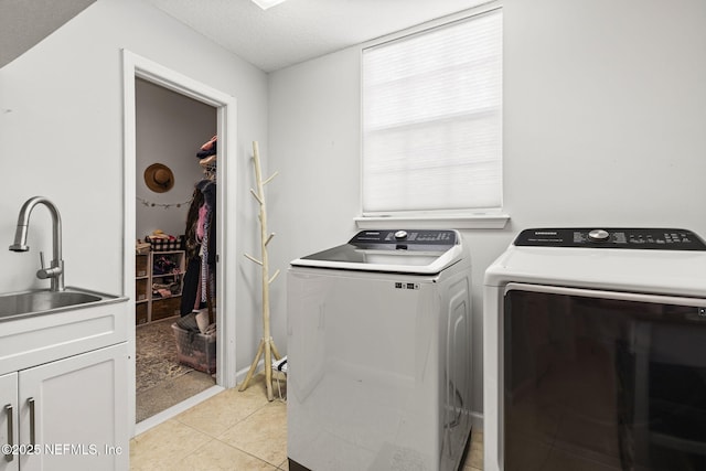 laundry area featuring light tile patterned flooring, sink, cabinets, washing machine and clothes dryer, and a textured ceiling