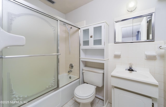 full bathroom with tile patterned flooring, tile walls, bath / shower combo with glass door, vanity, and toilet