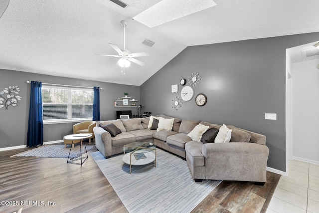 living area featuring lofted ceiling with skylight, wood finished floors, visible vents, and baseboards