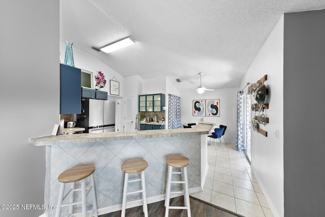 kitchen with light countertops, freestanding refrigerator, blue cabinets, a peninsula, and a kitchen breakfast bar