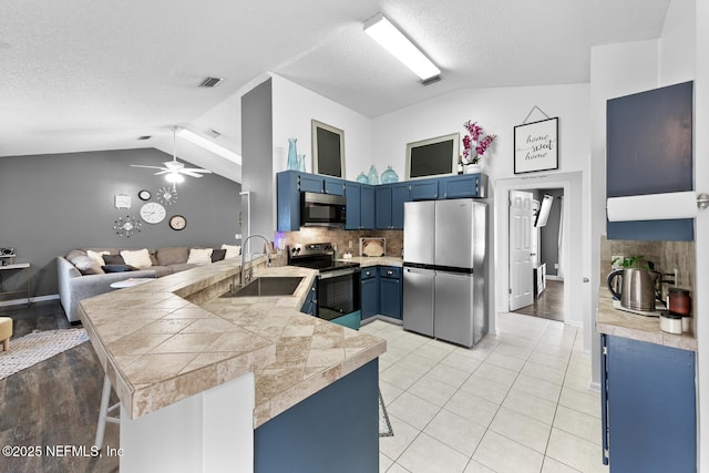 kitchen featuring lofted ceiling, appliances with stainless steel finishes, a sink, blue cabinets, and a peninsula