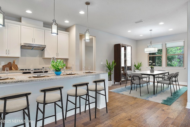 kitchen featuring a breakfast bar, white cabinetry, pendant lighting, light stone countertops, and hardwood / wood-style floors