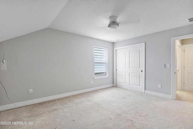 unfurnished bedroom featuring ceiling fan, a textured ceiling, vaulted ceiling, light colored carpet, and a closet