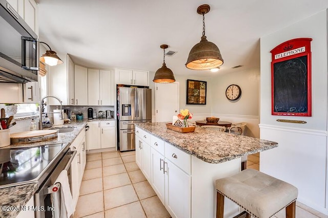 kitchen featuring appliances with stainless steel finishes, white cabinetry, a breakfast bar area, hanging light fixtures, and a center island