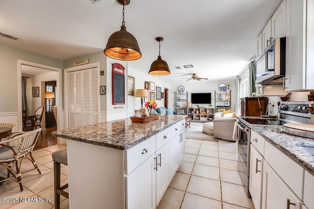 kitchen with white cabinetry, decorative light fixtures, appliances with stainless steel finishes, a kitchen island, and stone counters