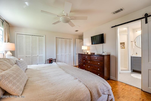 bedroom with connected bathroom, two closets, ceiling fan, light parquet flooring, and a barn door