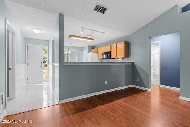 interior space featuring visible vents, light wood-style flooring, freestanding refrigerator, a textured ceiling, and black microwave