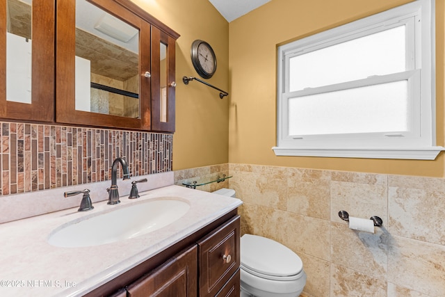 bathroom with tile walls, a wainscoted wall, vanity, and toilet