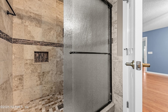 full bathroom featuring a textured ceiling, tiled shower, wood finished floors, and baseboards