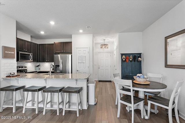 kitchen with sink, stainless steel appliances, tasteful backsplash, a kitchen bar, and light wood-type flooring