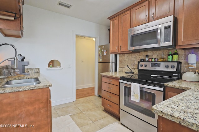 kitchen featuring sink, light tile patterned floors, stainless steel appliances, light stone countertops, and backsplash