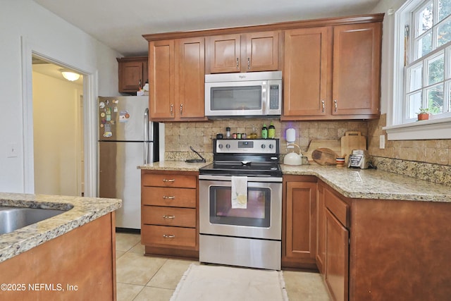 kitchen featuring stainless steel appliances, light tile patterned flooring, light stone countertops, and decorative backsplash