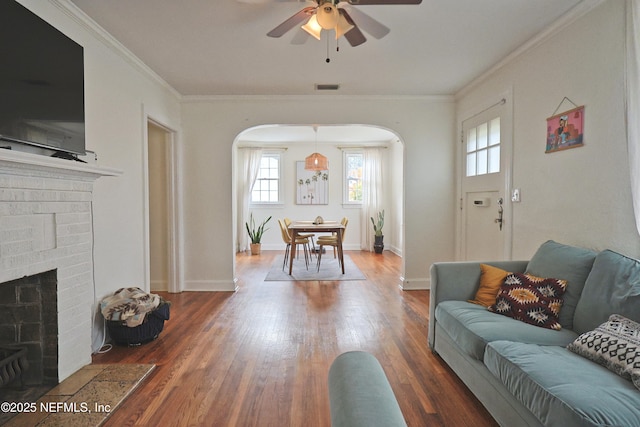 living room with dark wood-type flooring, ceiling fan, ornamental molding, and a fireplace