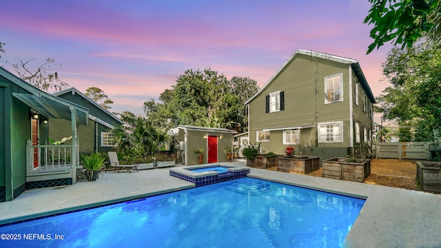 pool at dusk with a patio and an in ground hot tub