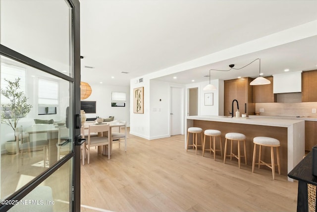 kitchen with a breakfast bar, sink, tasteful backsplash, light wood-type flooring, and pendant lighting