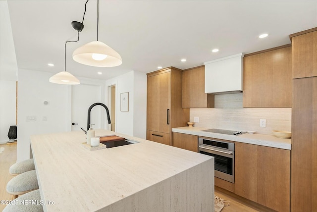 kitchen featuring sink, a center island with sink, black electric cooktop, pendant lighting, and oven