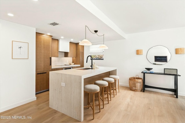 kitchen with pendant lighting, sink, an island with sink, and light hardwood / wood-style flooring