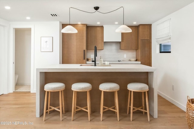 kitchen featuring hanging light fixtures, sink, backsplash, and light wood-type flooring