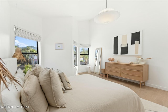 bedroom featuring a towering ceiling, light hardwood / wood-style floors, and multiple windows