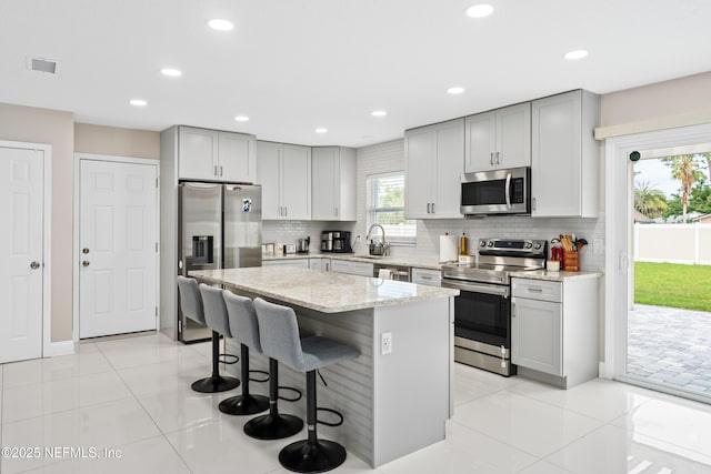 kitchen featuring light stone countertops, appliances with stainless steel finishes, a center island, and light tile patterned floors