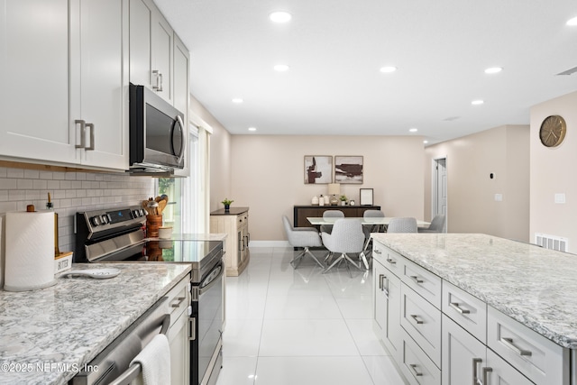 kitchen featuring tasteful backsplash, appliances with stainless steel finishes, light stone countertops, and light tile patterned floors