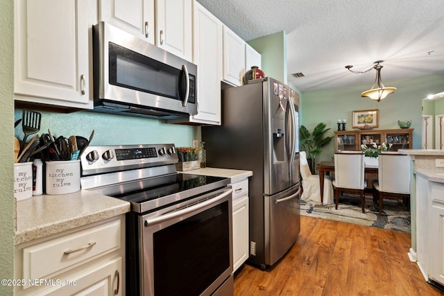 kitchen featuring white cabinetry, stainless steel appliances, decorative light fixtures, and a textured ceiling