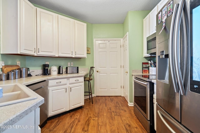 kitchen featuring hardwood / wood-style flooring, white cabinetry, appliances with stainless steel finishes, and a textured ceiling