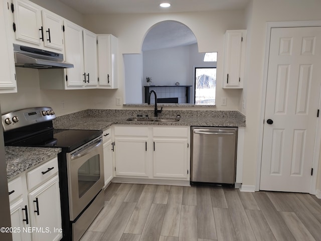 kitchen with white cabinets, stone counters, stainless steel appliances, under cabinet range hood, and a sink