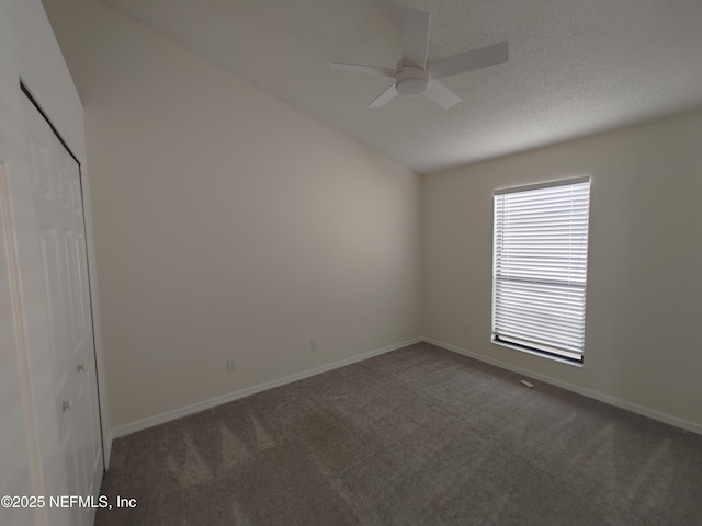 empty room featuring dark colored carpet, ceiling fan, a textured ceiling, and baseboards