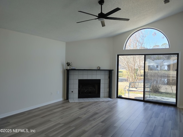 unfurnished living room with a textured ceiling, wood finished floors, plenty of natural light, and a tile fireplace