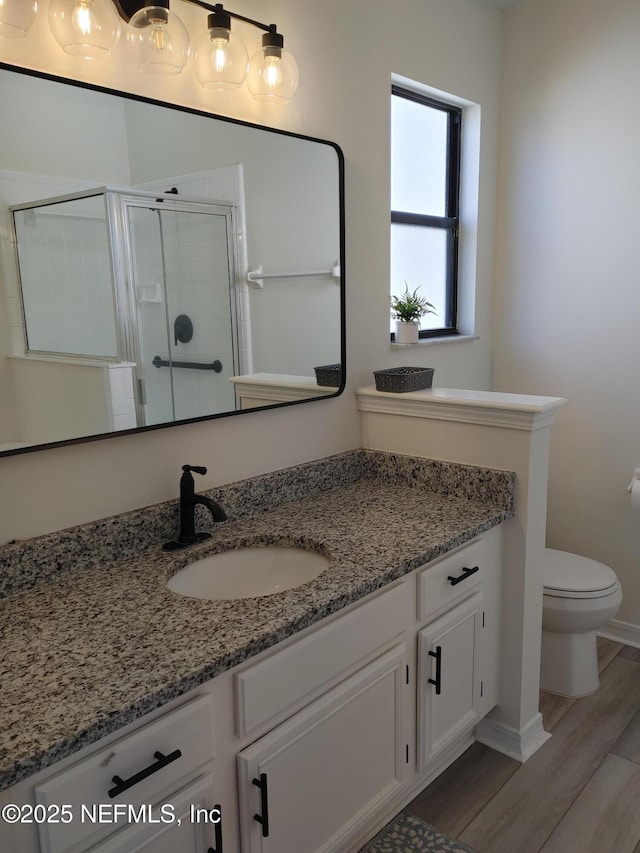 bathroom with a stall shower, vanity, toilet, and wood finished floors