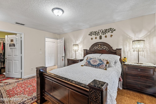 bedroom featuring a walk in closet, a textured ceiling, a closet, and light wood-type flooring