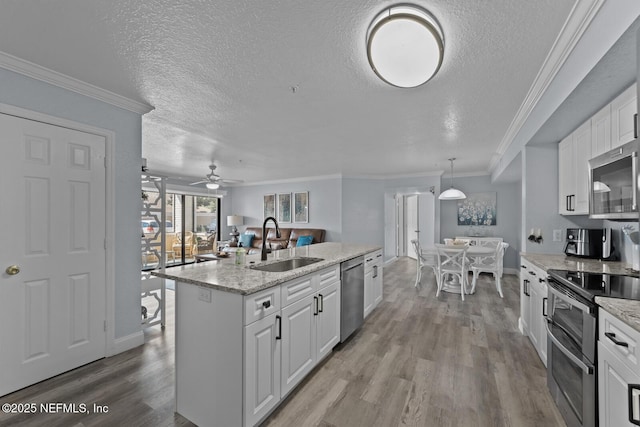 kitchen featuring a sink, white cabinetry, appliances with stainless steel finishes, light wood-type flooring, and a center island with sink