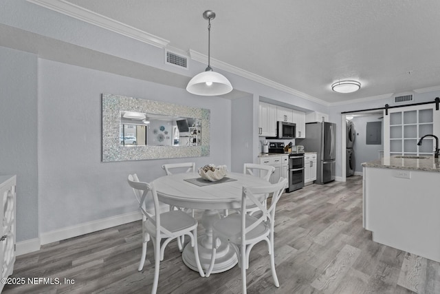 dining area with visible vents, a barn door, light wood finished floors, and stacked washer and clothes dryer