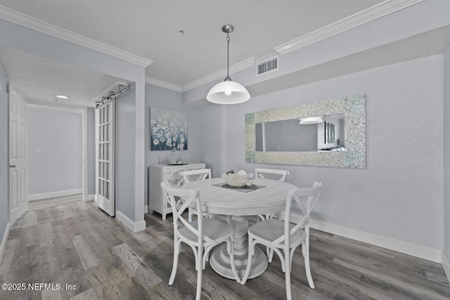 dining space with baseboards, a barn door, visible vents, and wood finished floors