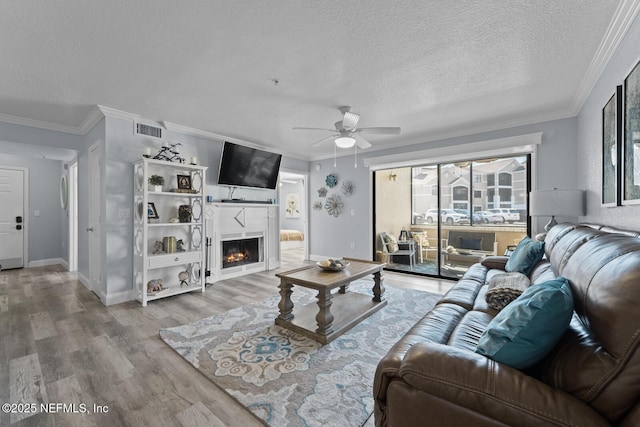 living area with visible vents, ornamental molding, a textured ceiling, wood finished floors, and a lit fireplace