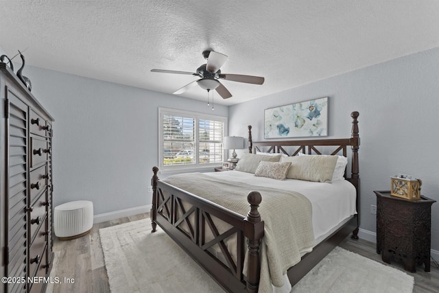 bedroom featuring ceiling fan, a textured ceiling, baseboards, and wood finished floors