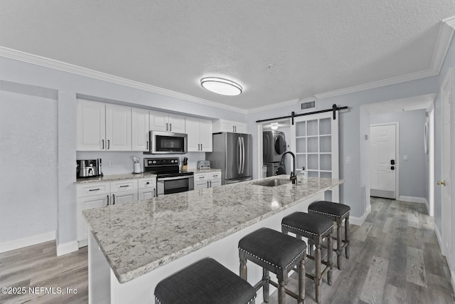 kitchen with a barn door, stainless steel appliances, wood finished floors, a sink, and stacked washer and clothes dryer