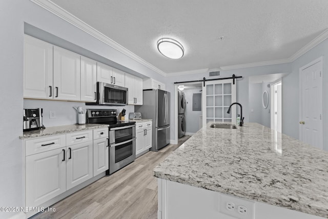 kitchen featuring a barn door, stacked washer / dryer, appliances with stainless steel finishes, white cabinetry, and a sink