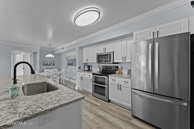 kitchen featuring a sink, light wood-style floors, white cabinets, ornamental molding, and appliances with stainless steel finishes