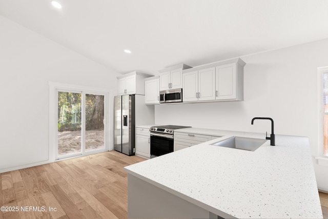 kitchen with light wood-style flooring, a peninsula, a sink, white cabinetry, and appliances with stainless steel finishes