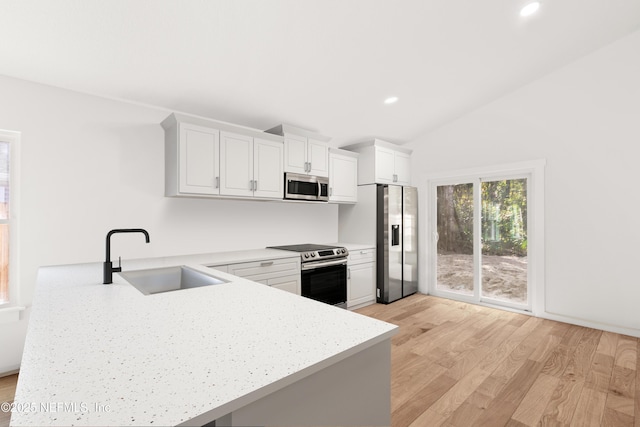 kitchen featuring a peninsula, a sink, vaulted ceiling, appliances with stainless steel finishes, and light wood finished floors