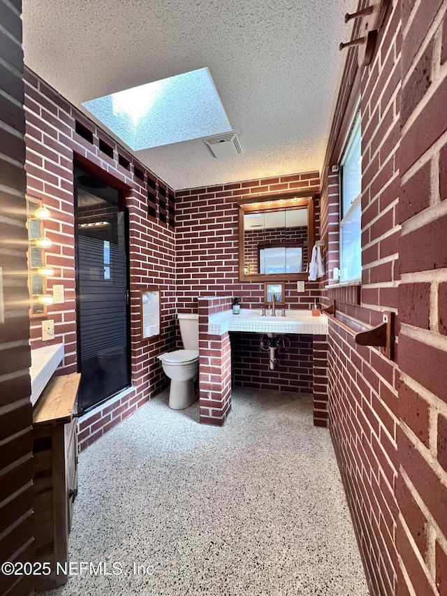 bathroom with brick wall, toilet, a shower with door, and a textured ceiling