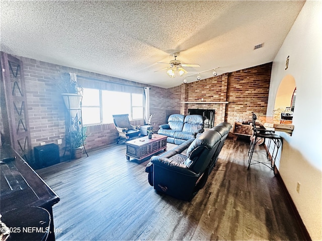 living room featuring vaulted ceiling, brick wall, hardwood / wood-style floors, a fireplace, and ceiling fan