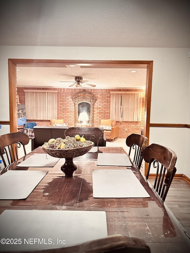 dining room featuring ceiling fan, brick wall, and a textured ceiling