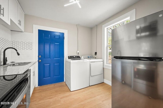 clothes washing area featuring washing machine and clothes dryer, sink, and light hardwood / wood-style flooring